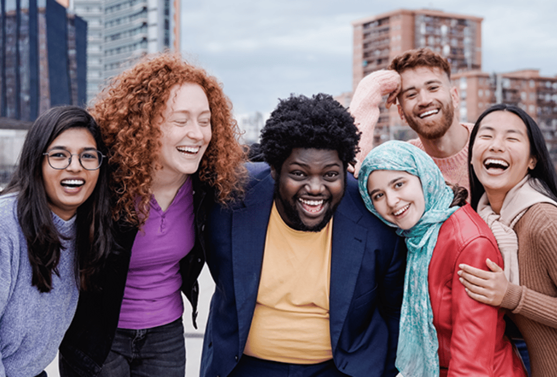 Six diverse friends smiling and posing together outdoors in an urban setting in the city district area of the photo.