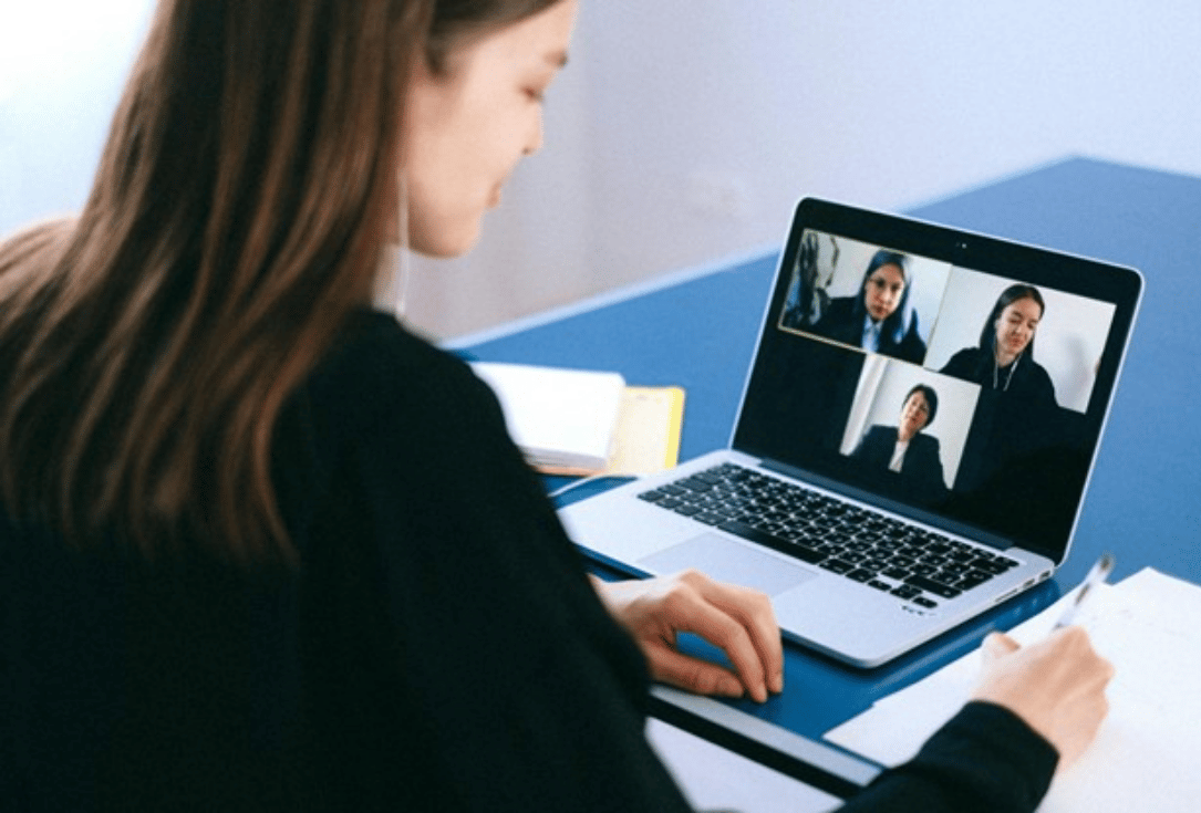 Woman taking notes during a four-way video conference on a laptop screen.