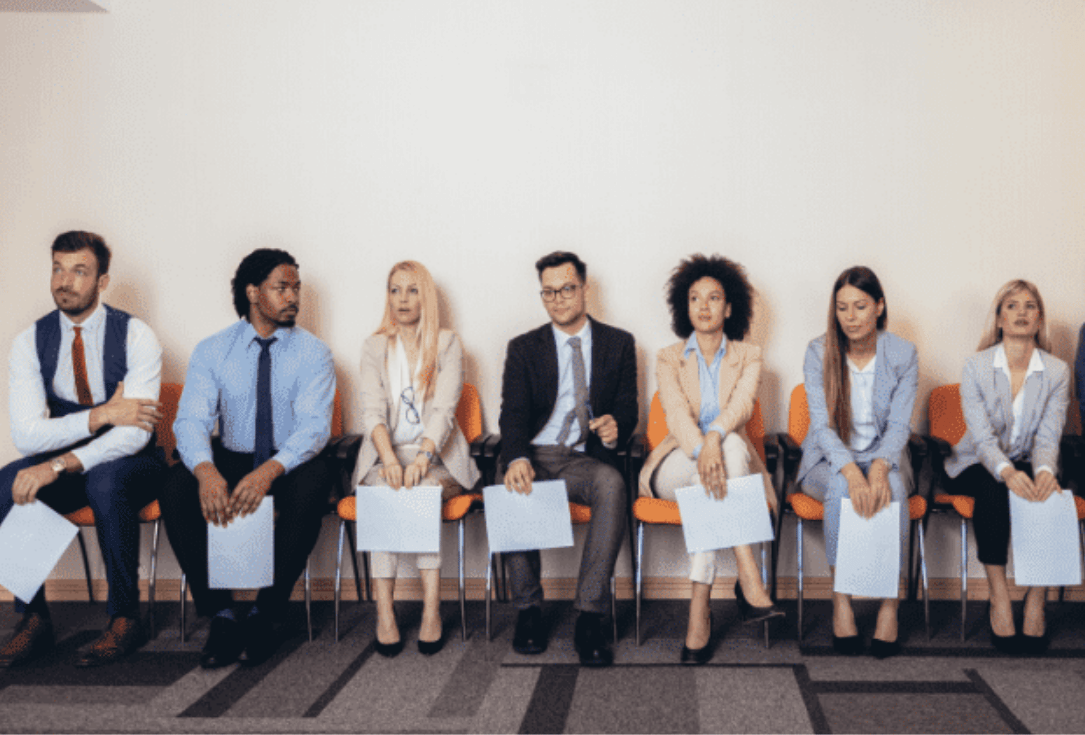 Row of job applicants seated in a waiting area, each holding a blue folder or clipboard before interviews.