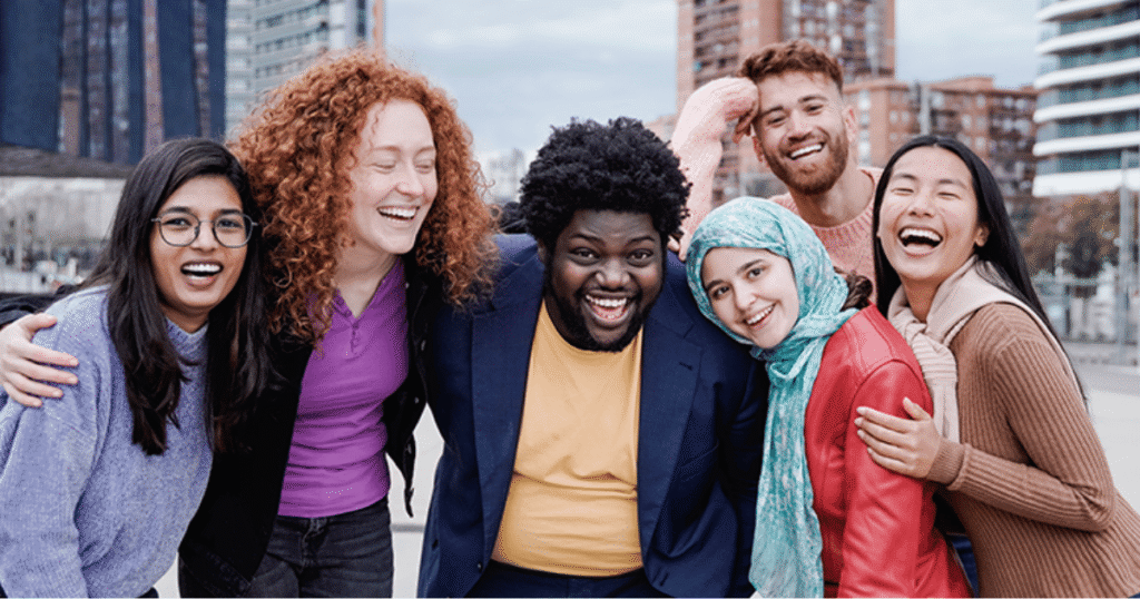 Diverse group of six friends smiling and posing together outdoors in an urban setting.