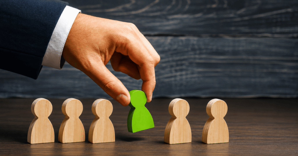 Hand placing a bright green wooden figure among beige figures, symbolizing candidate selection or recruitment.