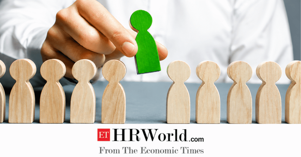 Hand selecting a green wooden figure from a row of natural wooden figurines, symbolizing recruitment, hiring, or leadership, with the ET HRWorld logo displayed at the bottom.