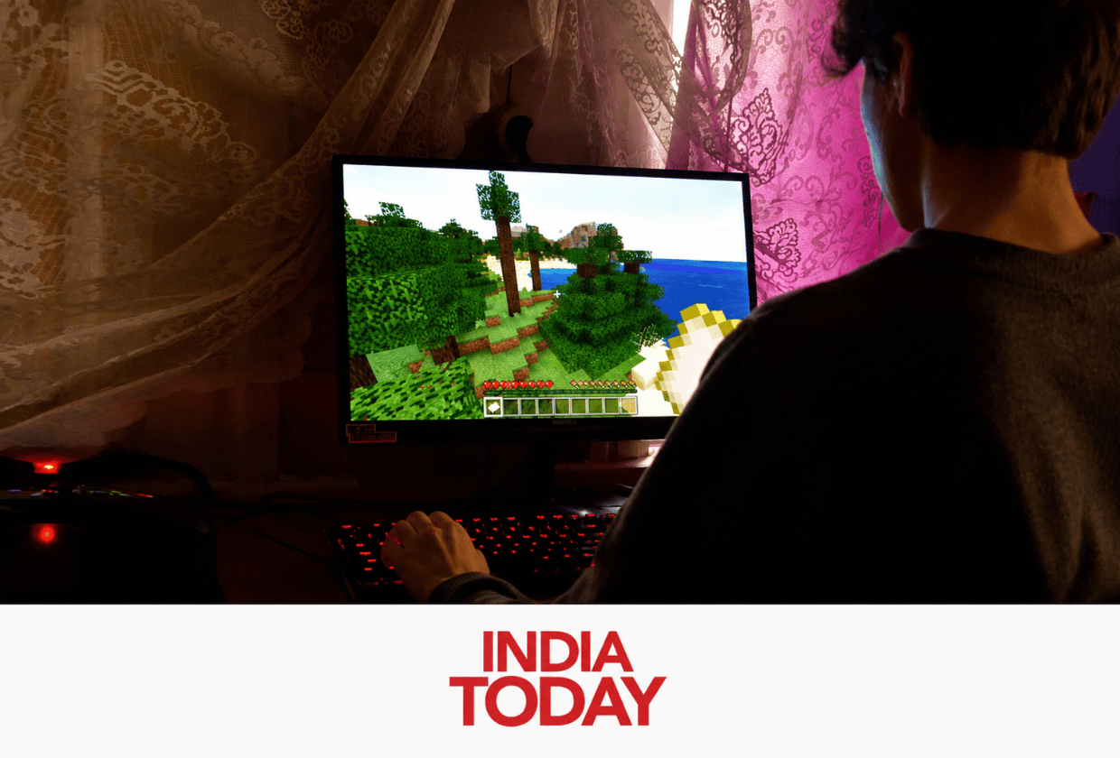 Person playing game on a desktop computer in a dimly lit room with lace curtains and a gaming setup, viewed from behind.