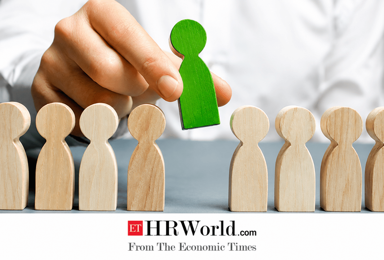 Hand selecting a green wooden figure from a row of natural wooden figurines, symbolizing recruitment, hiring, or leadership, with the ET HRWorld logo displayed at the bottom.