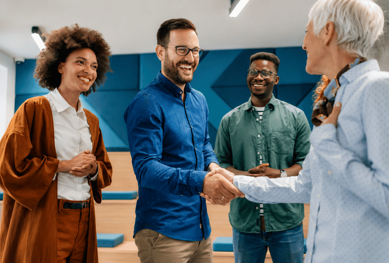 A diverse group of professionals smiling and shaking hands in a modern office, symbolizing a successful meeting, collaboration, and a positive workplace culture.