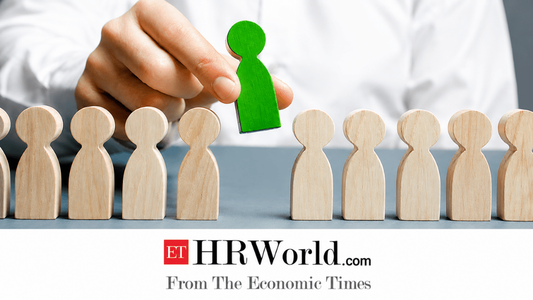 Green figure selected from a row of wooden silhouettes as a hand places it among them, symbolizing recruitment or selection, with HRWorld branding below.