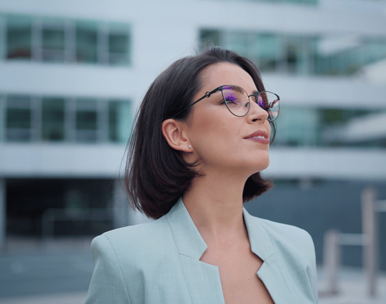Professional woman in glasses standing confidently outside a modern office building.